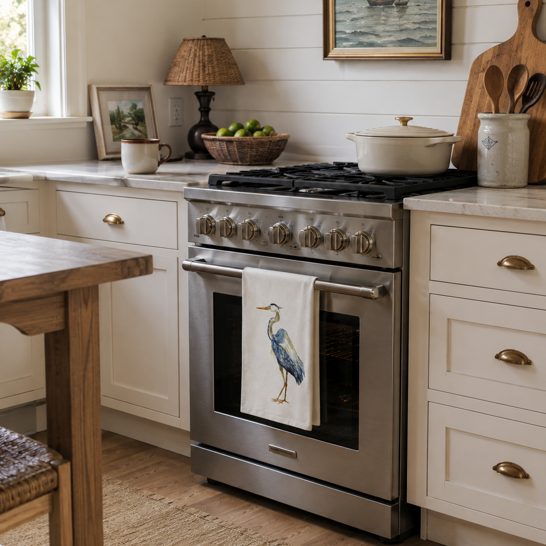 A stainless steel gas range stove in a bright, white shiplap kitchen, with a white towel featuring a blue heron printed on the oven door handle.