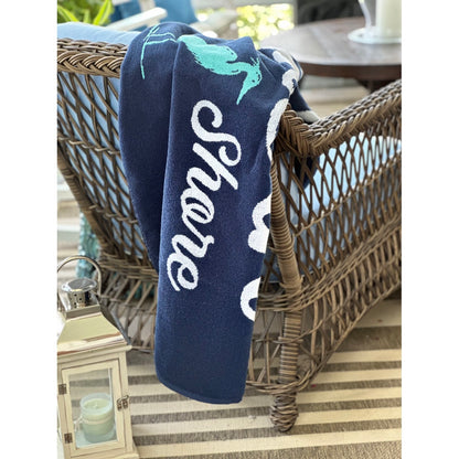 A navy blue towel draped over a wicker patio chair, featuring white cursive text reading &