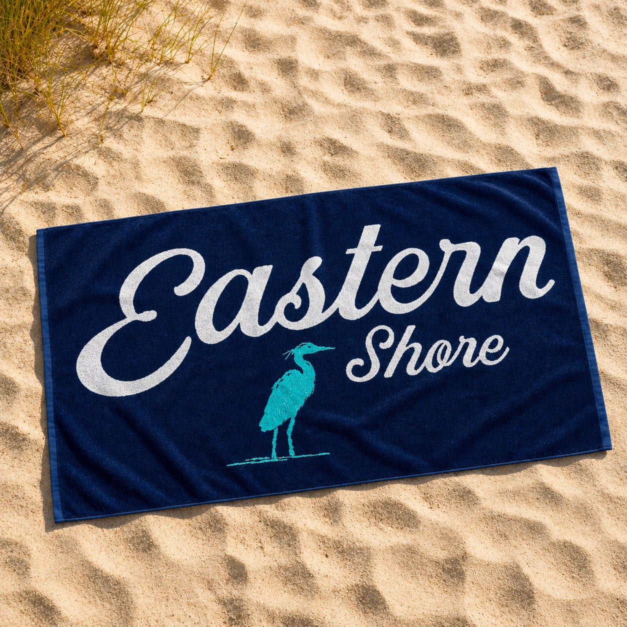 A navy blue beach towel laid flat on sandy ground, printed with the words &