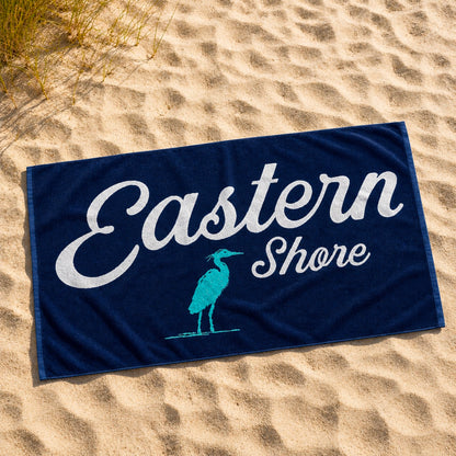 A navy blue beach towel laid flat on sandy ground, printed with the words &