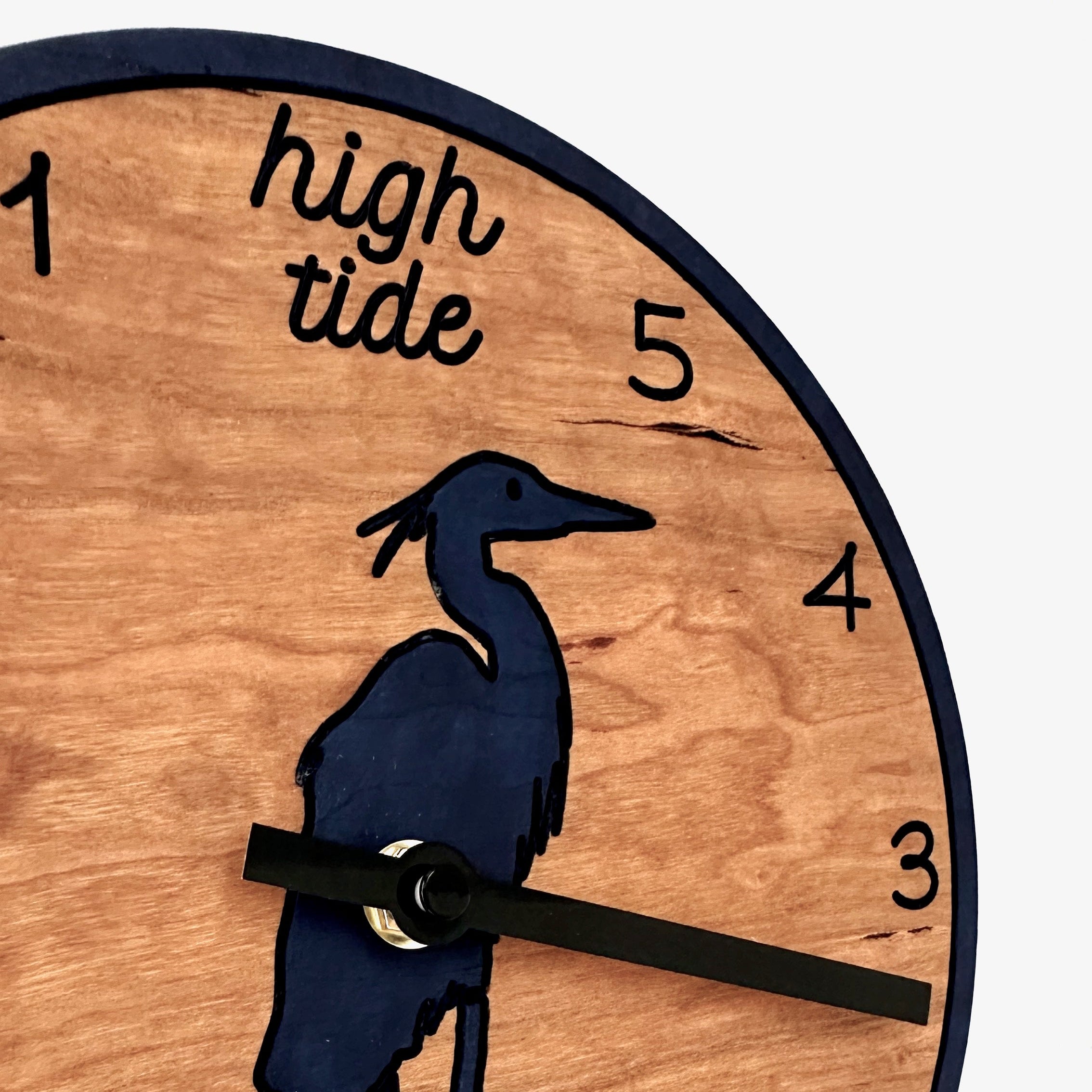A round wooden wall clock with a dark blue heron silhouette and black hands, featuring &